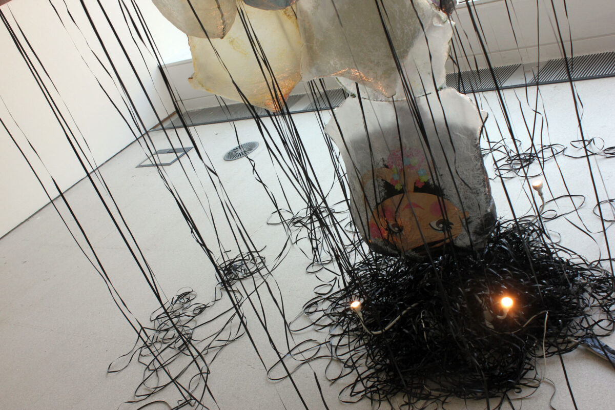 Close-up of GYRE installation showing black balloon ribbons pooled on the floor